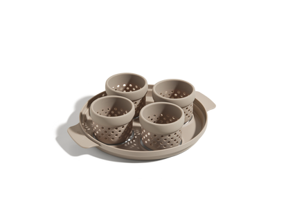 The Egg Poacher is a beige plastic tray with two handles, holding four matching perforated silicone cups, shown on a white background.