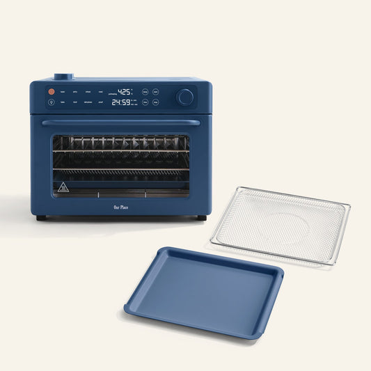 The Wonder Oven Pro + Wonder Oven Pro Essentials Kit features a blue countertop oven with a digital display, shown alongside a matching blue baking tray and a metal wire rack positioned in front.