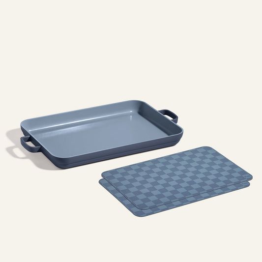 A Griddle Pan + Oven Mats set in blue, featuring a rectangular pan with handles, is displayed next to two stacked, blue checkered-pattern oven mats on a light background.