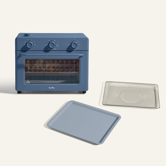 The Large Wonder Oven + Essentials Kit in blue features three control knobs, with a baking tray and wire rack displayed in front of it on a plain background.