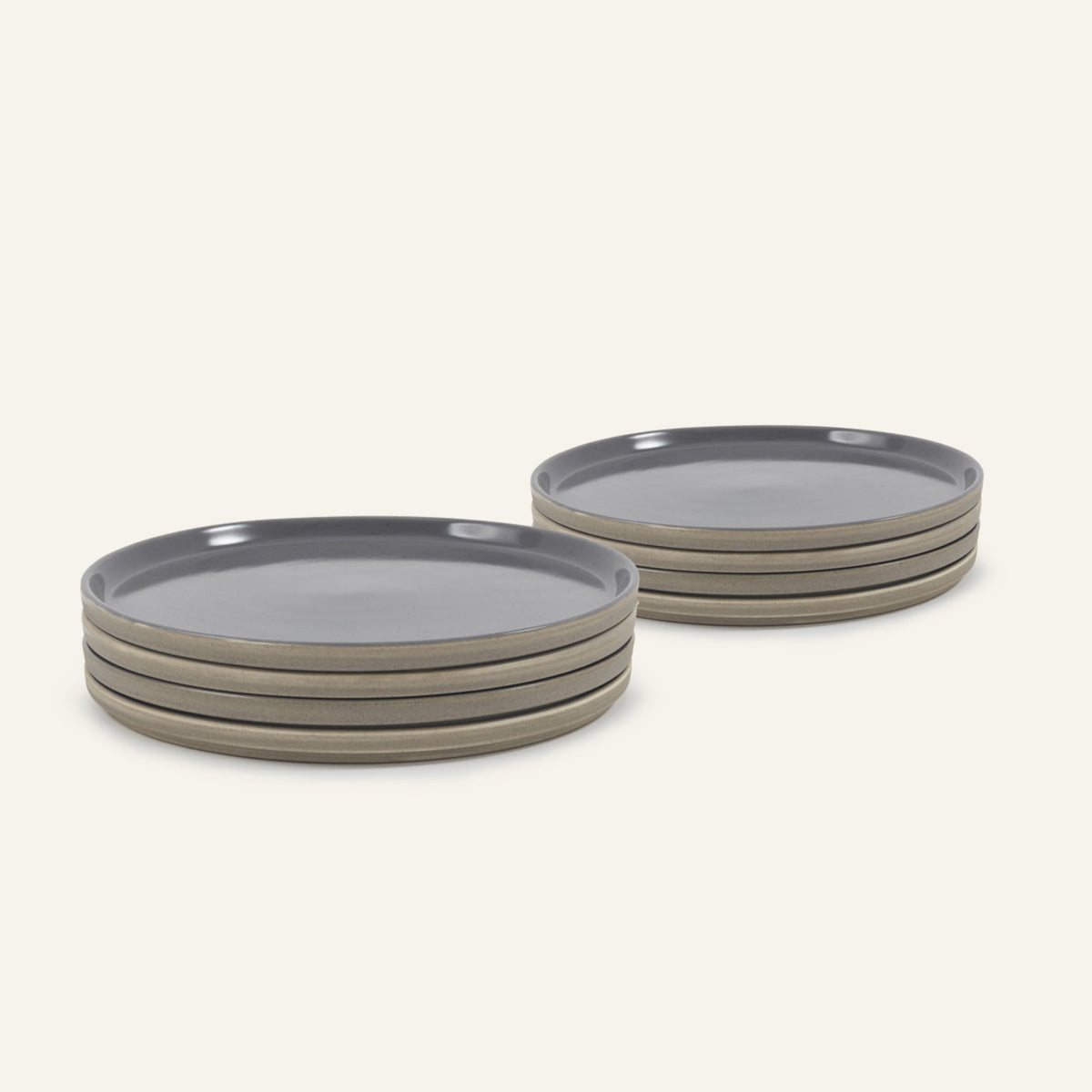 Two stacks of Main Plates, round and hand-painted gray with beige sides, are arranged on a light background. Each stack has four plates, highlighting a modern minimalist style that’s both functional and stylish.