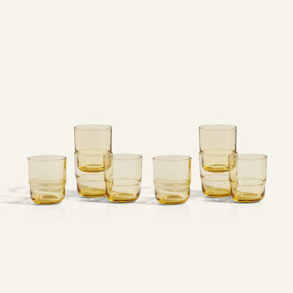 Six amber-tinted Short Night + Day Glasses, handcrafted from recycled glass, are arranged in two rows on a light background—some stacked—showcasing their artisanal charm.