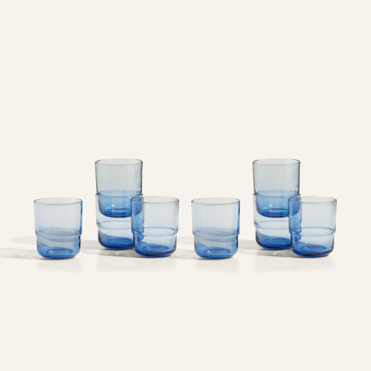 Six Short Night + Day Glasses, made from transparent blue recycled glass, are arranged in pairs on a plain light background.