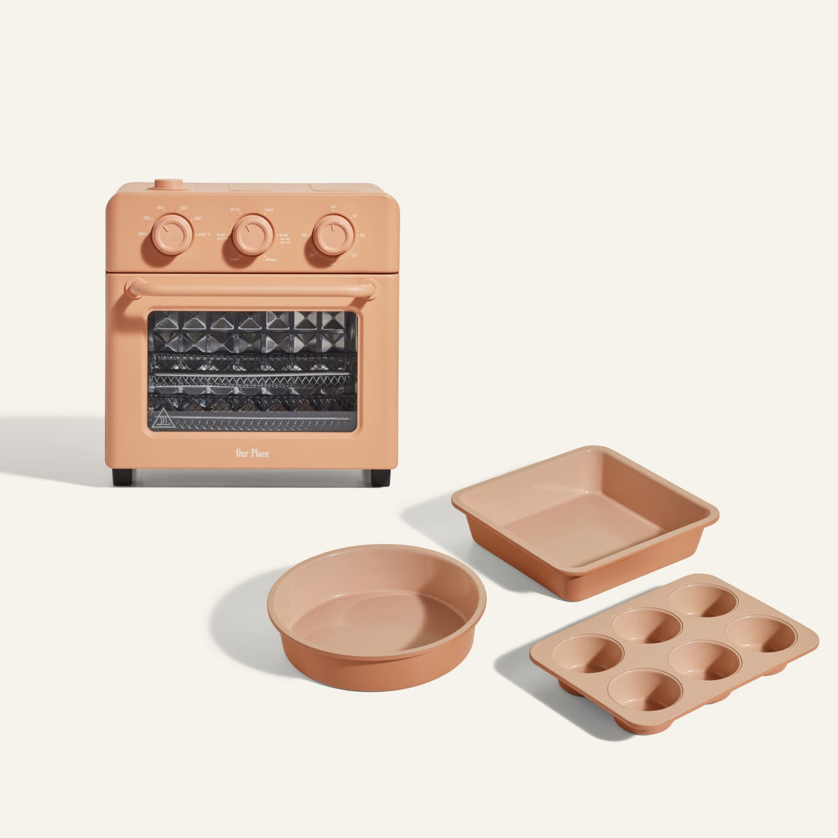Wonder Oven + Wonder Oven Baker's Kit in peach includes a countertop oven with three control knobs, plus matching baking pans: a square pan, round pan, and six-cup muffin tray, all shown against a plain background.