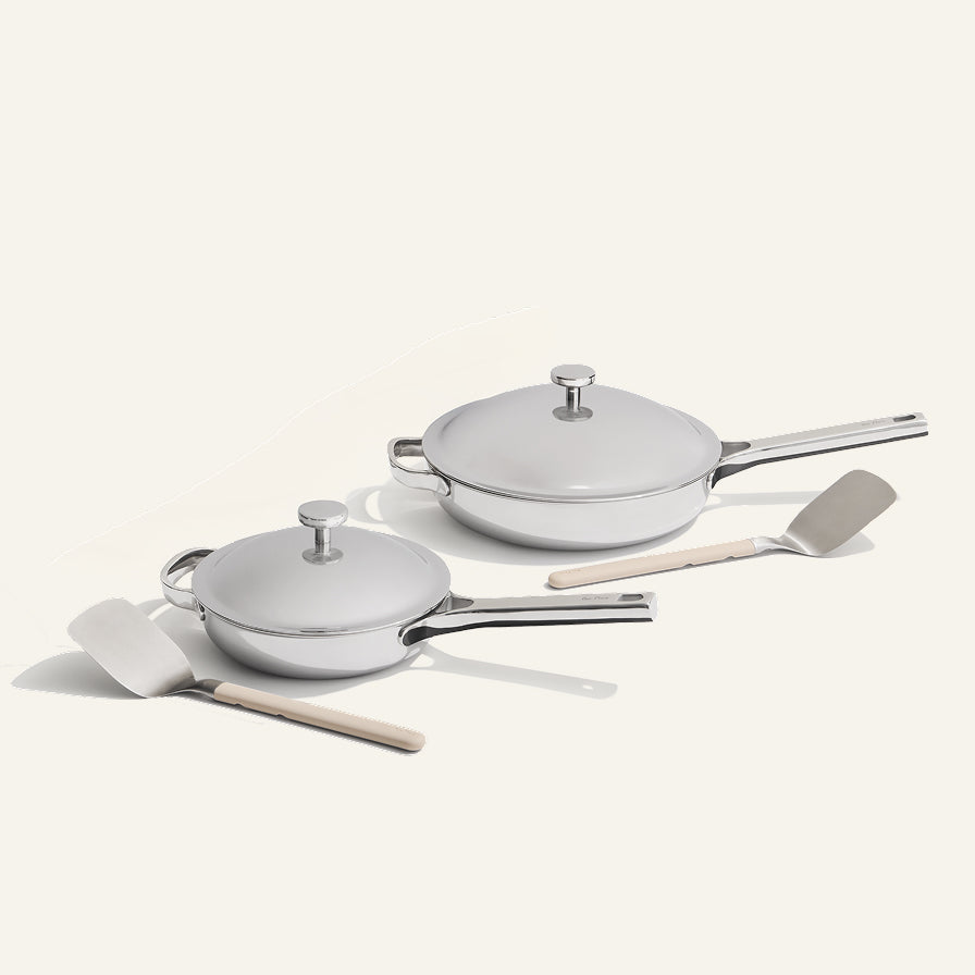 Set of white cookware with lids and wooden spatulas on a light gray background