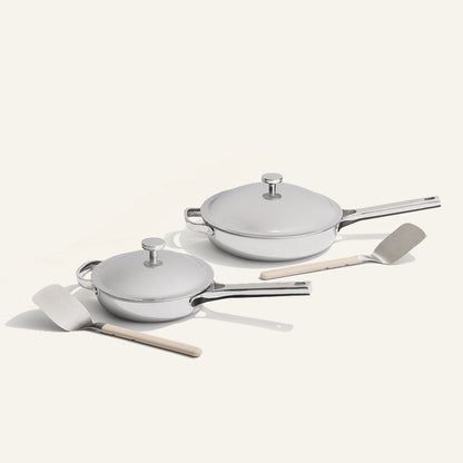 Set of white cookware with lids and wooden spatulas on a light gray background